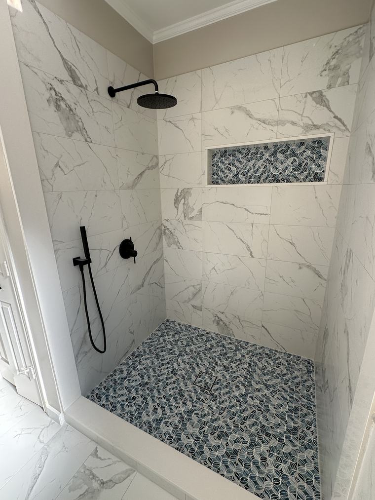 White marble shower with black fixtures and a blue mosaic tile niche and floor