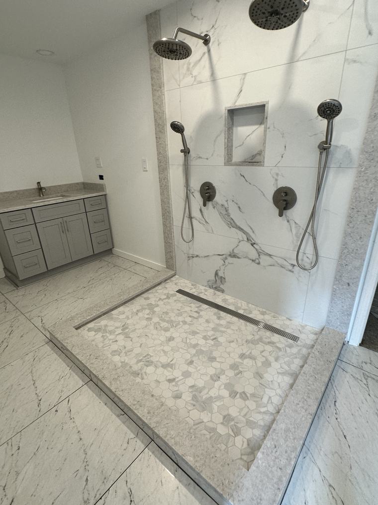 Walk-in marble shower with dual shower heads, tile niche, and hexagon mosaic floor