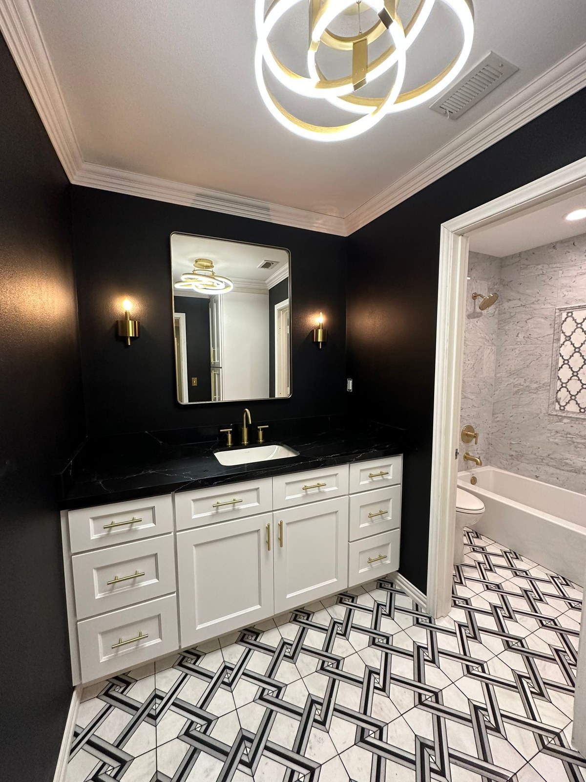 Bathroom with white cabinetry, black counters, gold fixtures, and a geometric black-and-white tile floor