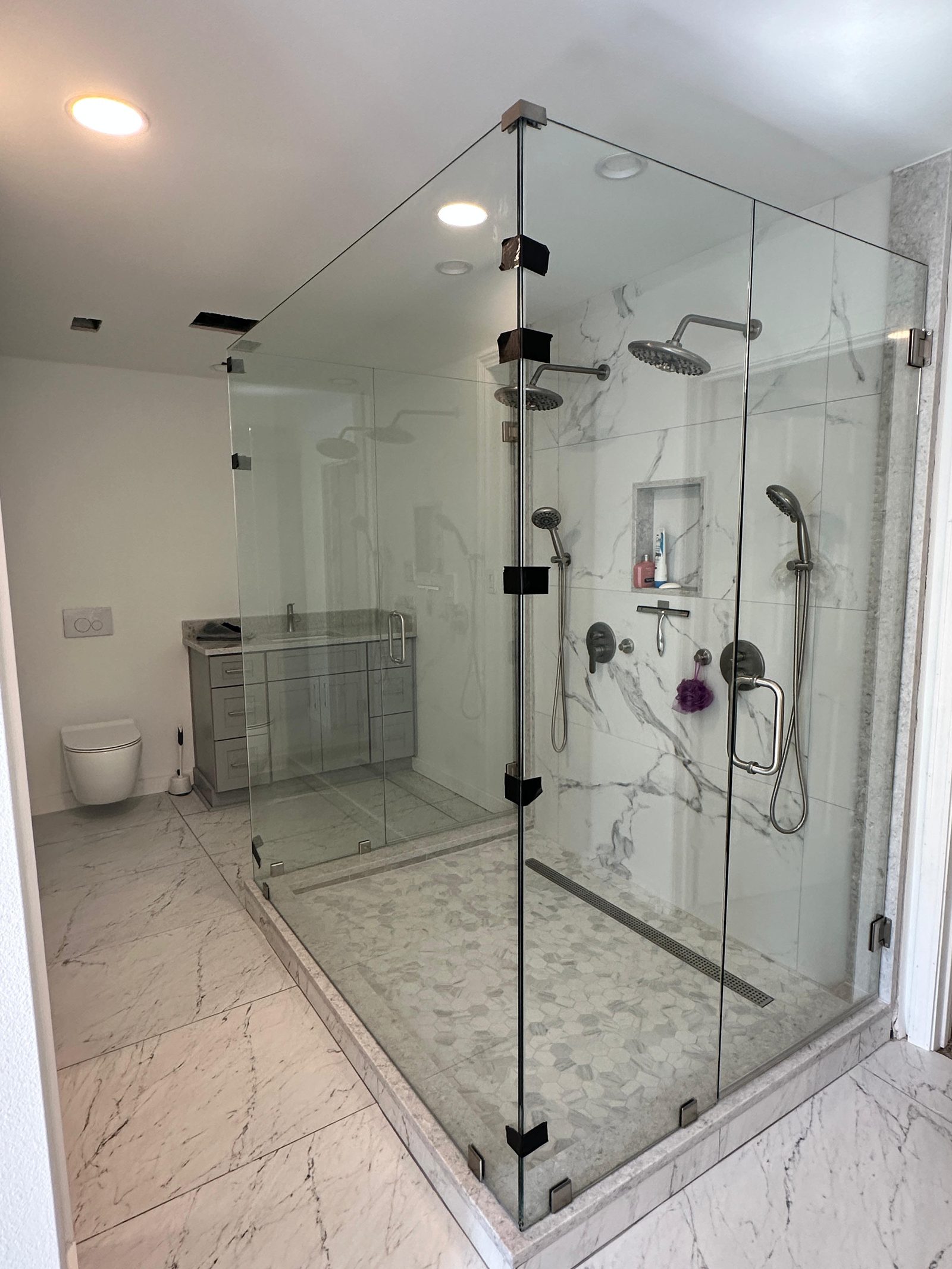Frameless glass corner shower with dual rain heads, marble slab walls, and hexagon mosaic floor